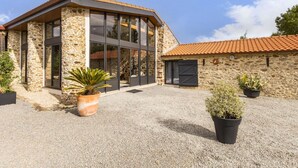 A modern building with stone walls and large windows, surrounded by gravel and potted plants. - "Charming Cottage with Private Garden, Jacuzzi, and Bikes – Near Nantes & Beach" (Port-Saint-Père)