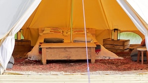 Een tent met een bed, houten nachtkastjes en een lantaarn.