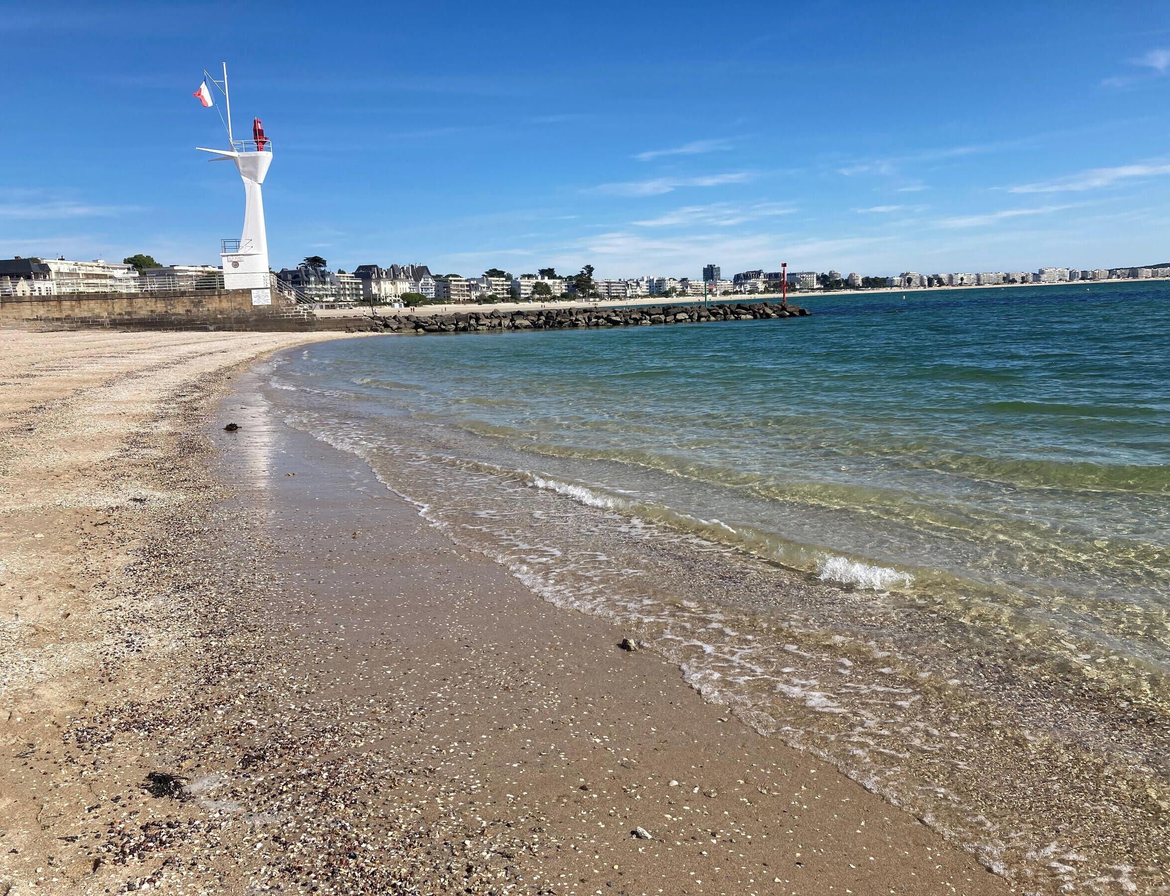 Een strand met een vuurtoren, helder water en een rotsachtige kustlijn.