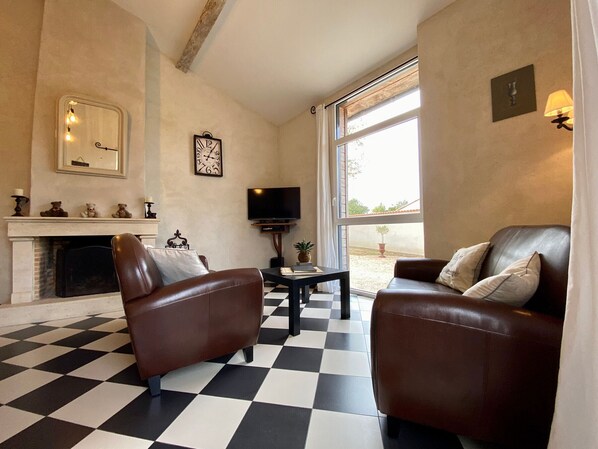 A living room with a checkered floor, two leather sofas, a fireplace, a television, and a large window.
