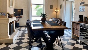 Ein Essbereich mit Schachbrettmuster-Boden, einem Holztisch, schwarzen Stühlen, einer Ananas als Mittelpunkt und einem Fernseher auf einem Standfuß.
