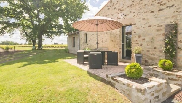 Ein Steinhaus mit einer Terrassenfläche, ausgestattet mit Tisch, Stühlen, Sonnenschirm und Kübelpflanzen.