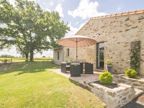 A stone building with a patio area featuring a table and chairs, an umbrella, and potted plants.