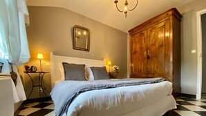 Ein Schlafzimmer mit einem Bett, einem Holzschrank, einem an der Wand befestigten Spiegel, zwei Nachttischen mit Lampen und einem Schachbrettfußboden.