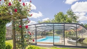 Ein von Glas umschlossener Pool mit gewölbtem Dach, umgeben von Grünpflanzen und einer Steinmauer.