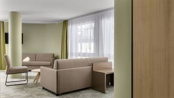 Ein modernes Hotelzimmer mit einer beigefarbenen Sofagarnitur, einem kleinen Tisch und einem Stuhl.