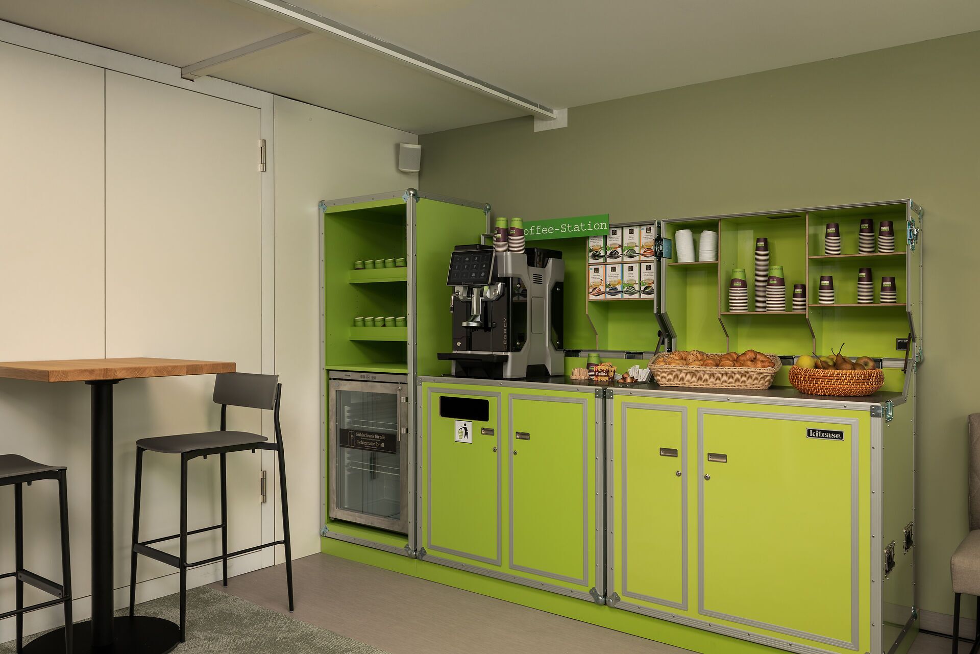 A kitchenette with a coffee station, a refrigerator, and a seating area with two chairs.