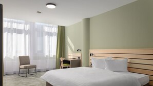 A hotel room with a large bed, a desk, a chair, and a window with sheer curtains. - flexy.motel Buchs (Buchs)