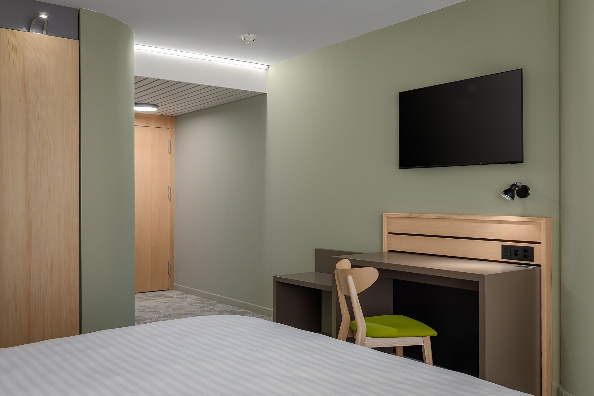 A hotel room with a bed, a desk with a chair, a television, and a wardrobe.