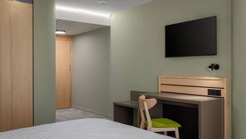 Una habitación de hotel con cama, escritorio, silla, televisor y armario.