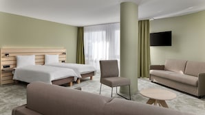 A hotel room with two beds, a sofa, a chair, a small table, and a TV mounted on the wall. - flexy.motel Buchs (Buchs)