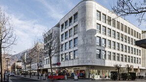 A modern building with a curved facade, multiple windows, and a ground-level retail space. - flexy.motel Buchs (Buchs)