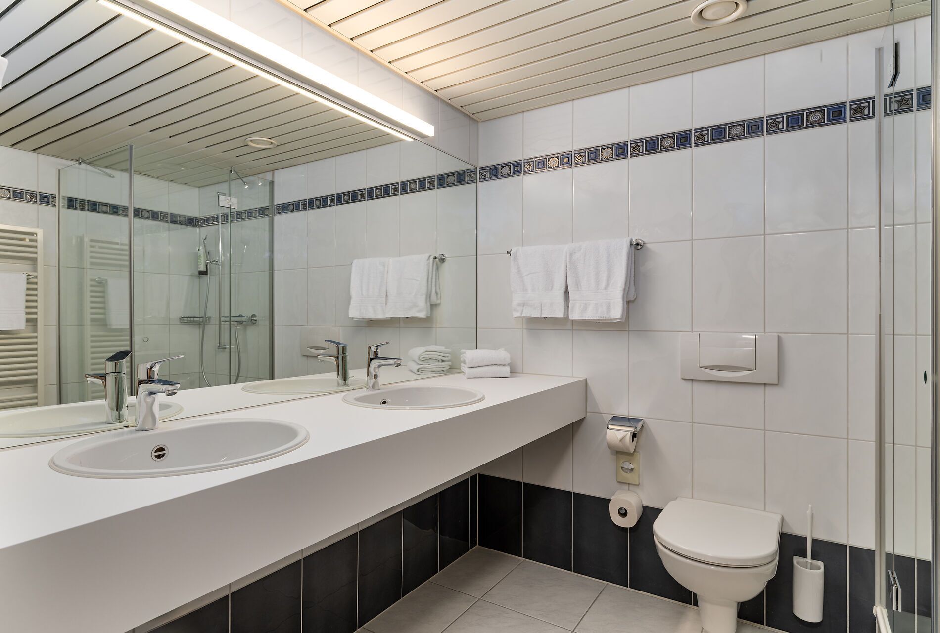 Ein modernes Badezimmer mit zwei Waschbecken, einer Toilette und einer Dusche.