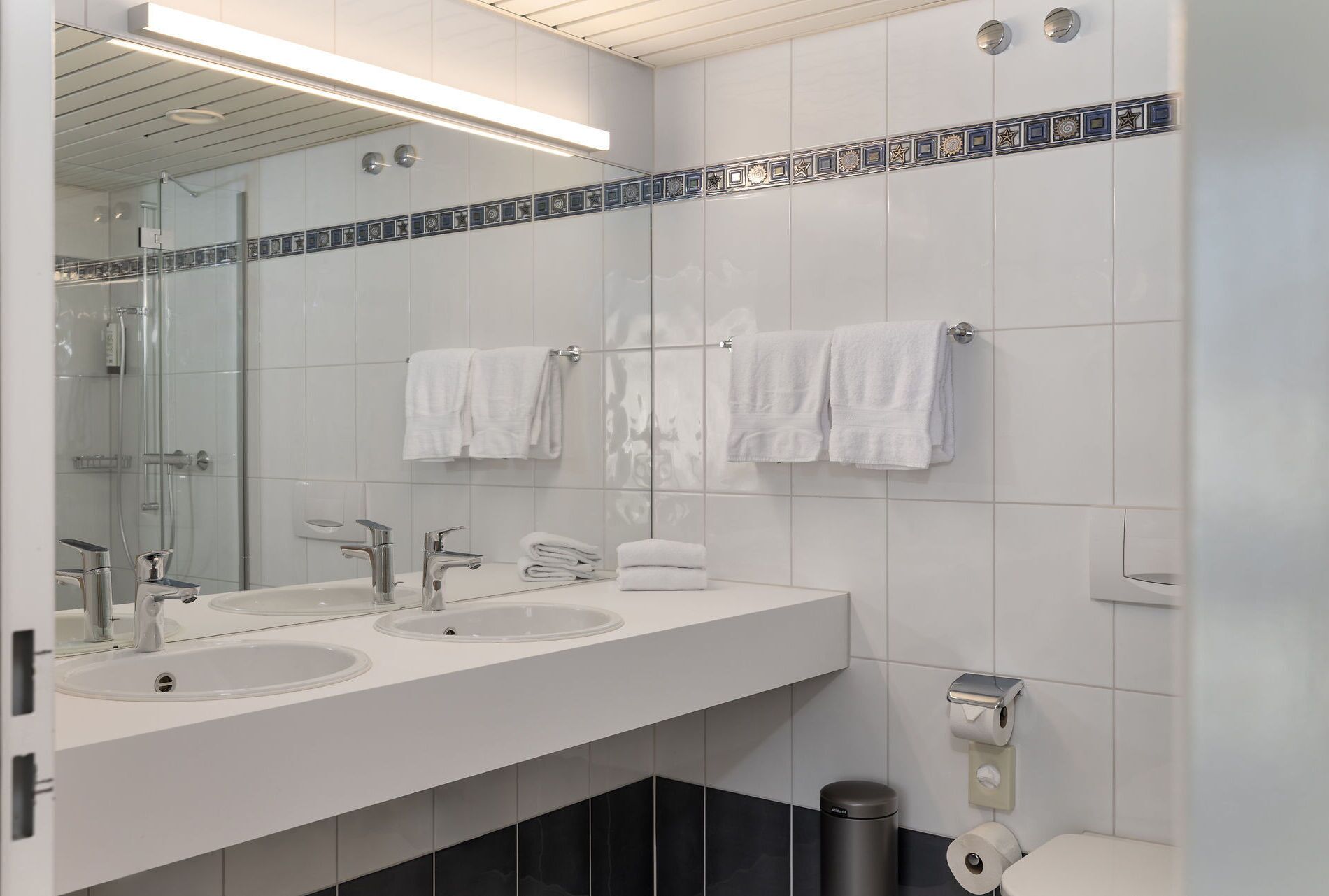 A modern bathroom with two sinks, a glass shower enclosure, and a toilet.