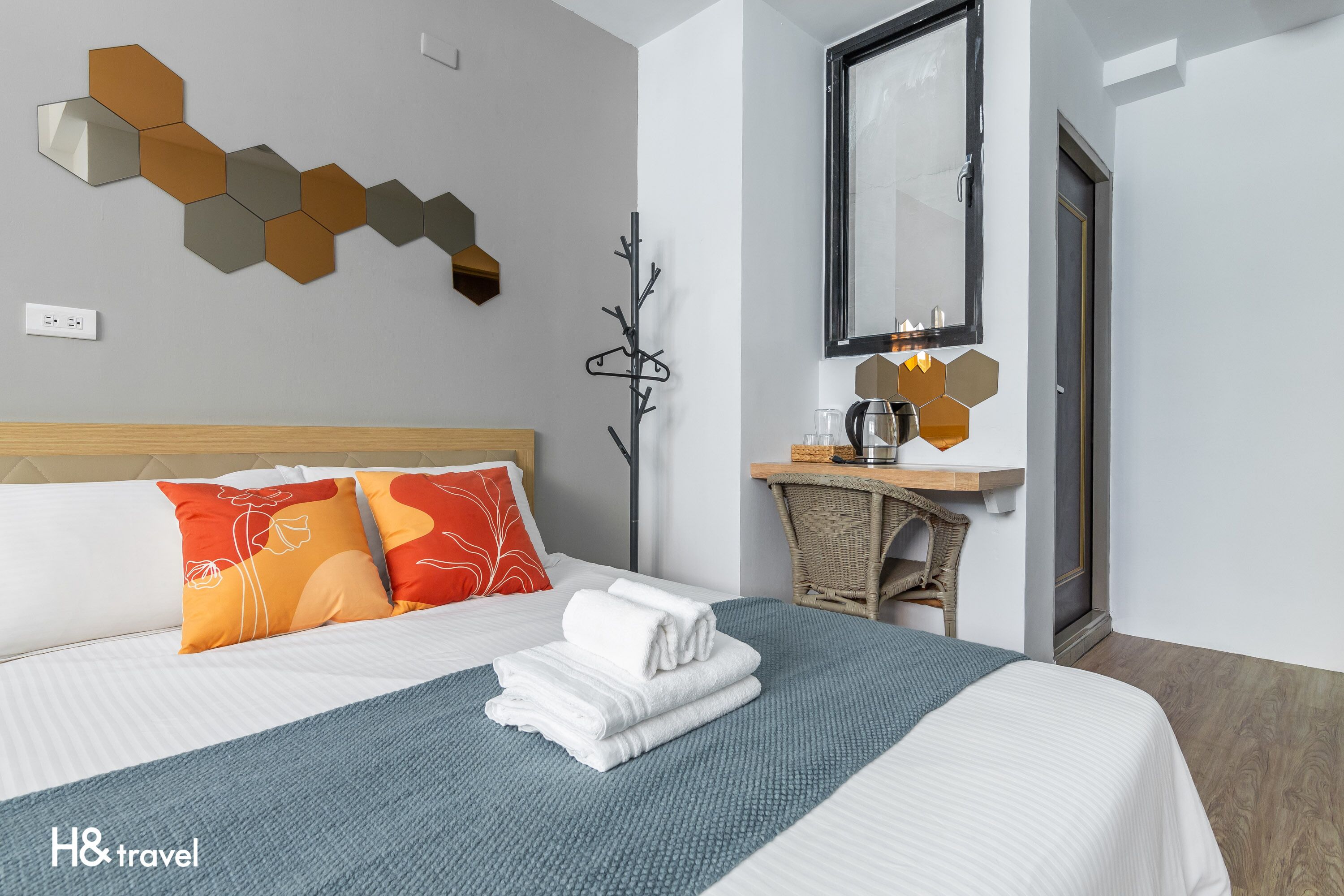 A hotel room with a neatly made bed, a wall-mounted mirror, a small table with a coffee pot, and a wall art piece.