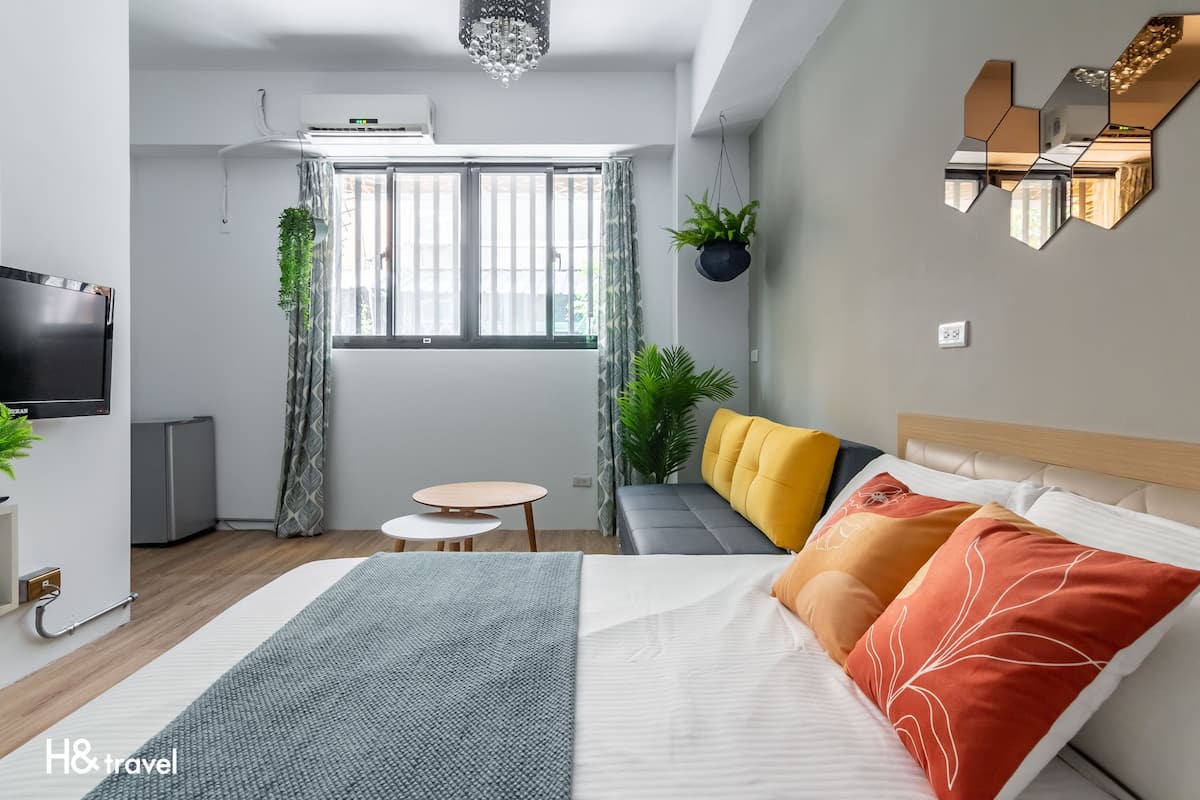 Quarto de hotel moderno com uma cama grande, um sofá, uma mesinha e uma televisão.