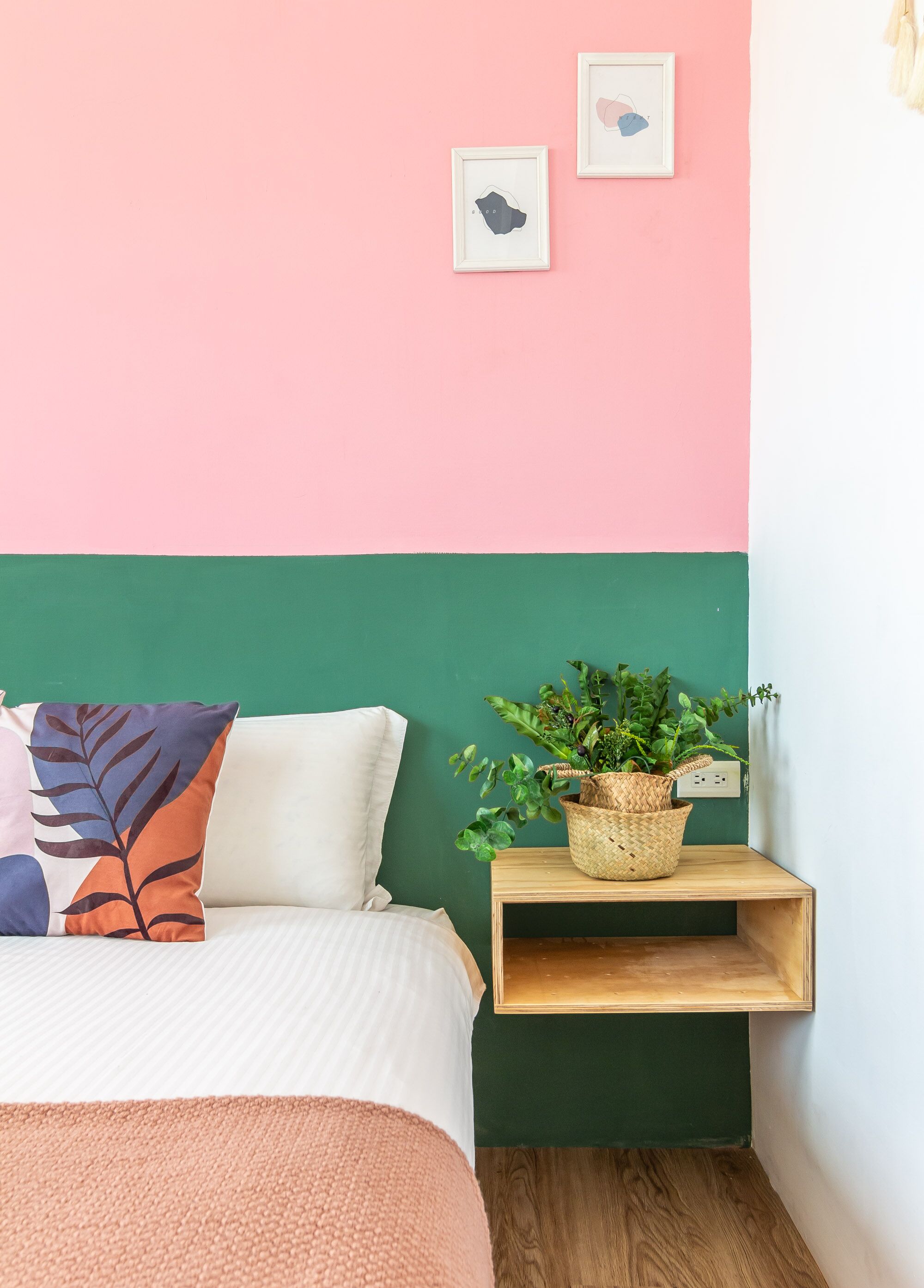 Une chambre à coucher avec un lit, des oreillers, une table de chevet avec une plante, et un mur orné de deux tableaux encadrés.