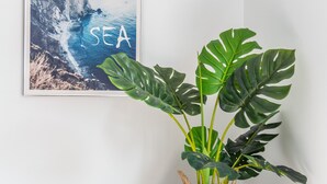 A framed coastal landscape artwork with the word "SEA" on a wall, a large monstera plant in a woven basket, and a pendant light. - Sleepier Multi-Minsu Tainan (Tainan)