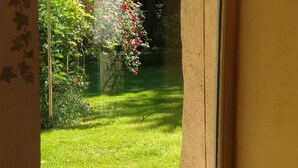 A view through a window of a well-maintained garden with a lawn and flowering plants. - Charming Cottage in Verdant Park with Modern Amenities & Family Activities (Nozay)
