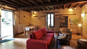 A cozy living room with a red sofa, a dining table set for four, and a bookshelf. - Charming Cottage in Verdant Park with Modern Amenities & Family Activities (Nozay)