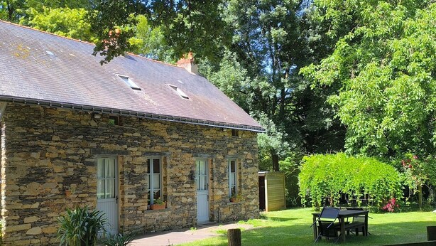 A stone house with a sloped roof, multiple windows, and a small garden area with a table and chairs. - Charming Cottage in Verdant Park with Modern Amenities & Family Activities (Nozay)
