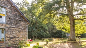 A stone building with a gravel driveway, surrounded by trees and a wooden fence. - Charming Cottage in Verdant Park with Modern Amenities & Family Activities (Nozay)