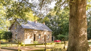 A stone house with a fenced yard, surrounded by trees. - Charming Cottage in Verdant Park with Modern Amenities & Family Activities (Nozay)