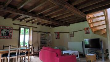 Un salon rustique avec des poutres apparentes, un canapé rouge, une table à manger avec des chaises, un téléviseur et des œuvres d’art accrochées aux murs.