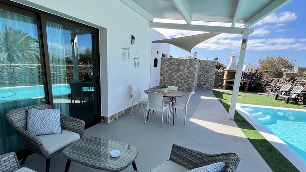Una terrazza esterna con mobili in vimini, una piscina e un muro in pietra.