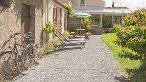 A gravel path leading to a patio area with a table and chairs, a bicycle, and a building with a window and door.