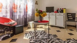 A modern living room with a red chair, a zebra-patterned rug, a small round table with a vase of flowers, and a TV on a cabinet. - Cozy Countryside Cottage near Brière Park with Garden, WiFi, and Modern Amenities (Missillac)