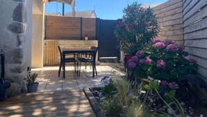 A patio area with a table and chairs, a wooden fence, and a potted plant with pink flowers. - Charming Renovated Cottage Near Beaches and Shops with Private Garden and Modern Amenities (Batz-sur-Mer)