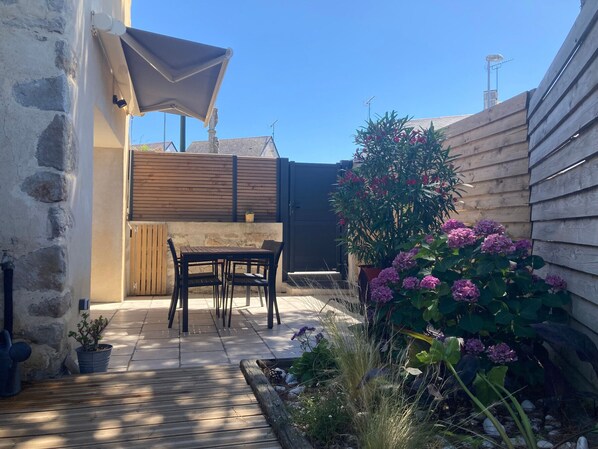 A patio area with a table and chairs, a wooden fence, and a potted plant with pink flowers. - Charming Renovated Cottage Near Beaches and Shops with Private Garden and Modern Amenities (Batz-sur-Mer)