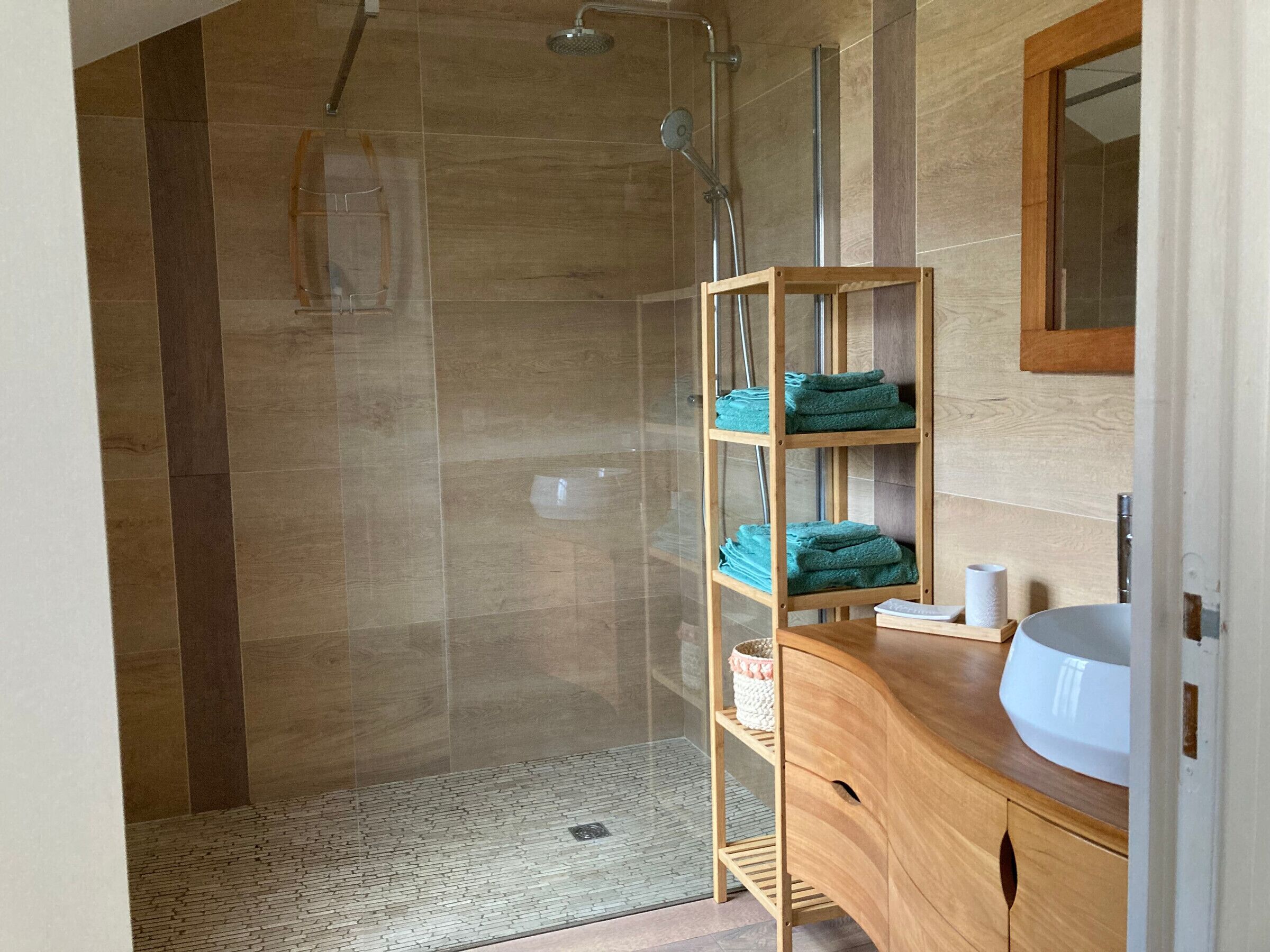 Une salle de bain moderne avec une douche à parois de verre, un meuble-lavabo en bois et une étagère où sont pliés les serviettes.