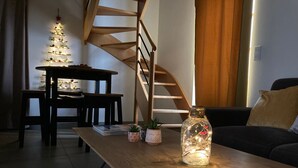 A modern living room with a wooden coffee table, a glass bottle with fairy lights, a staircase, and a Christmas tree. - Charming Renovated Cottage Near Beaches and Shops with Private Garden and Modern Amenities (Batz-sur-Mer)