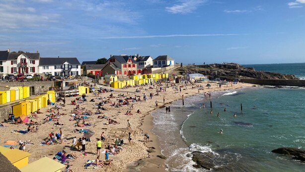 A beach with colorful buildings, a sandy shore, and clear blue water. - Charming Renovated Cottage Near Beaches and Shops with Private Garden and Modern Amenities (Batz-sur-Mer)