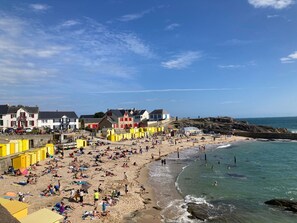 A beach with colorful buildings, a sandy shore, and clear blue water. - Charming Renovated Cottage Near Beaches and Shops with Private Garden and Modern Amenities (Batz-sur-Mer)