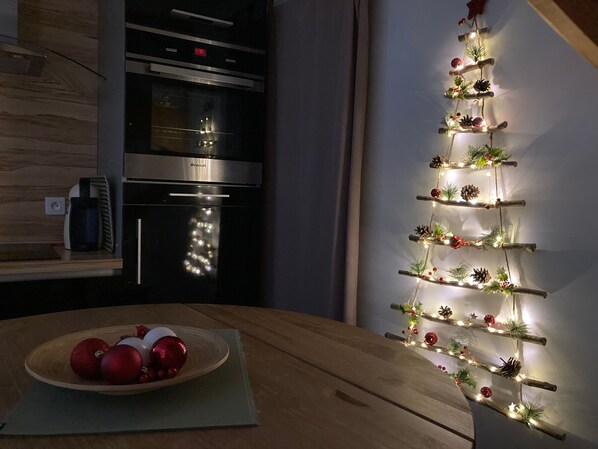 A kitchen with a wooden table, a plate of red ornaments, and a wall-mounted Christmas decoration. - Charming Renovated Cottage Near Beaches and Shops with Private Garden and Modern Amenities (Batz-sur-Mer)
