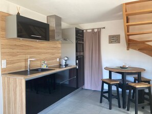 A compact kitchen with a modern design, featuring a sink, stove, and a small dining area with stools. - Charming Renovated Cottage Near Beaches and Shops with Private Garden and Modern Amenities (Batz-sur-Mer)