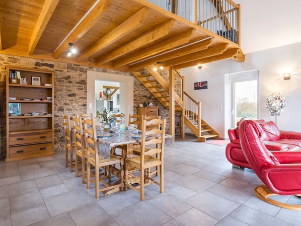A dining area with a wooden table and chairs, a red leather sofa, a staircase, and a stone wall.