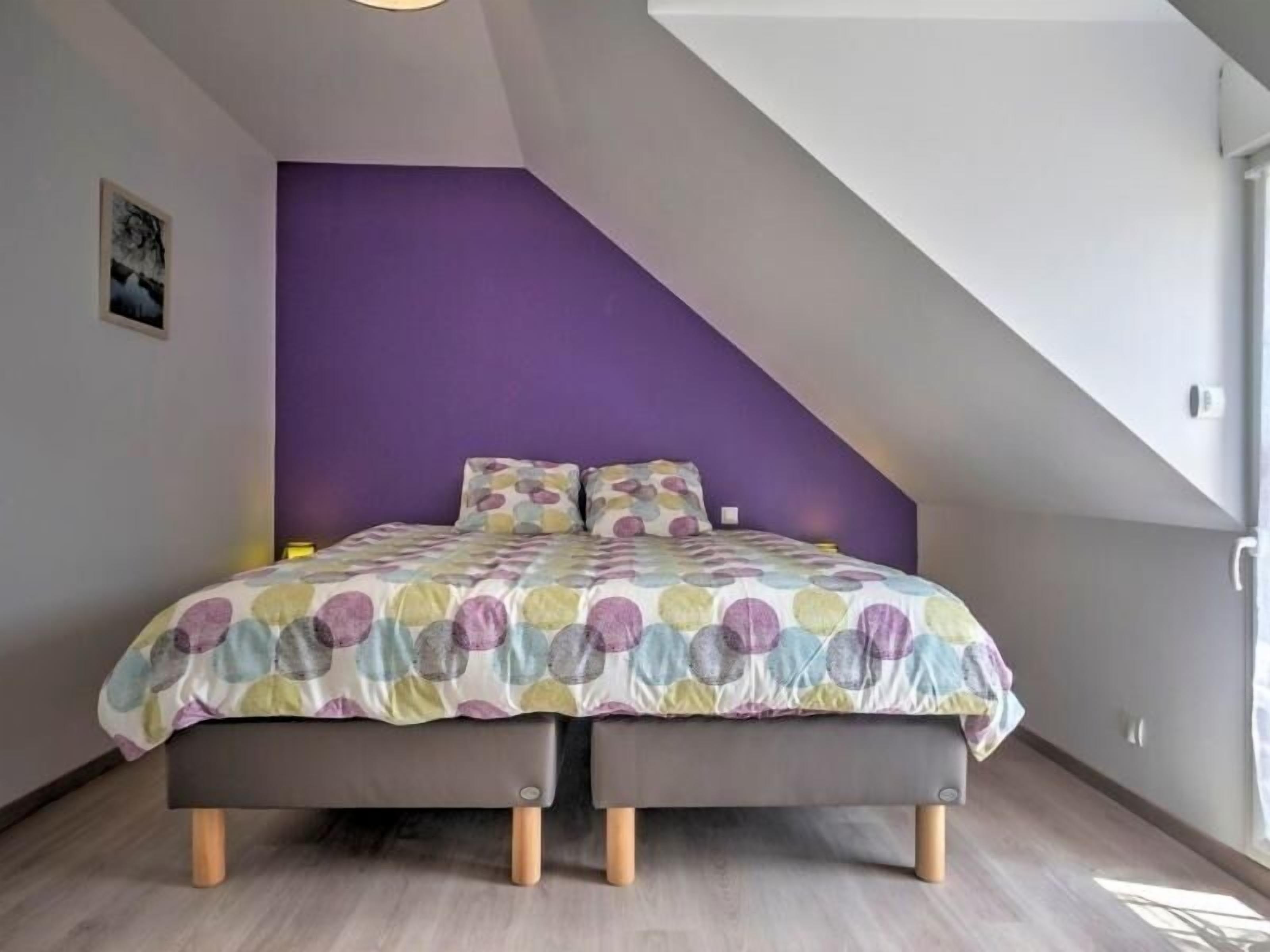 Een slaapkamer met een bed, een paarse accentmuur en een schuine plafond.
