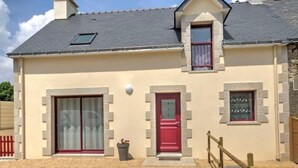 A two-story house with a red door, a small balcony, and a window with a decorative grille.