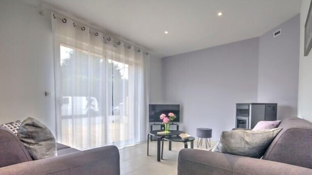A modern living room with two sofas, a TV, a small table with a vase, and a sliding glass door.