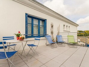 A terrace with a white building, blue shutters, and a table with a potted plant. - Cozy Coastal Retreat: 500m from Beach, Spacious Terrace, Free Parking, Wi-Fi, and Baby Amenities (Batz-sur-Mer)