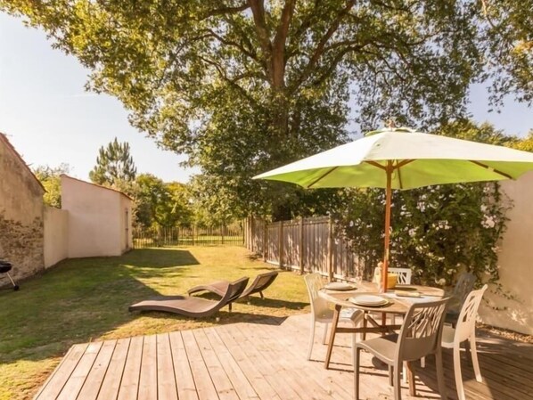 A wooden deck with a table and chairs, a green umbrella, and lounge chairs.