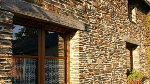 A stone building with a wooden door and windows, featuring a stone wall and a small window with a view of the sky.