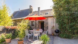 A stone house with a patio area featuring a table and chairs, surrounded by potted plants and a red umbrella.