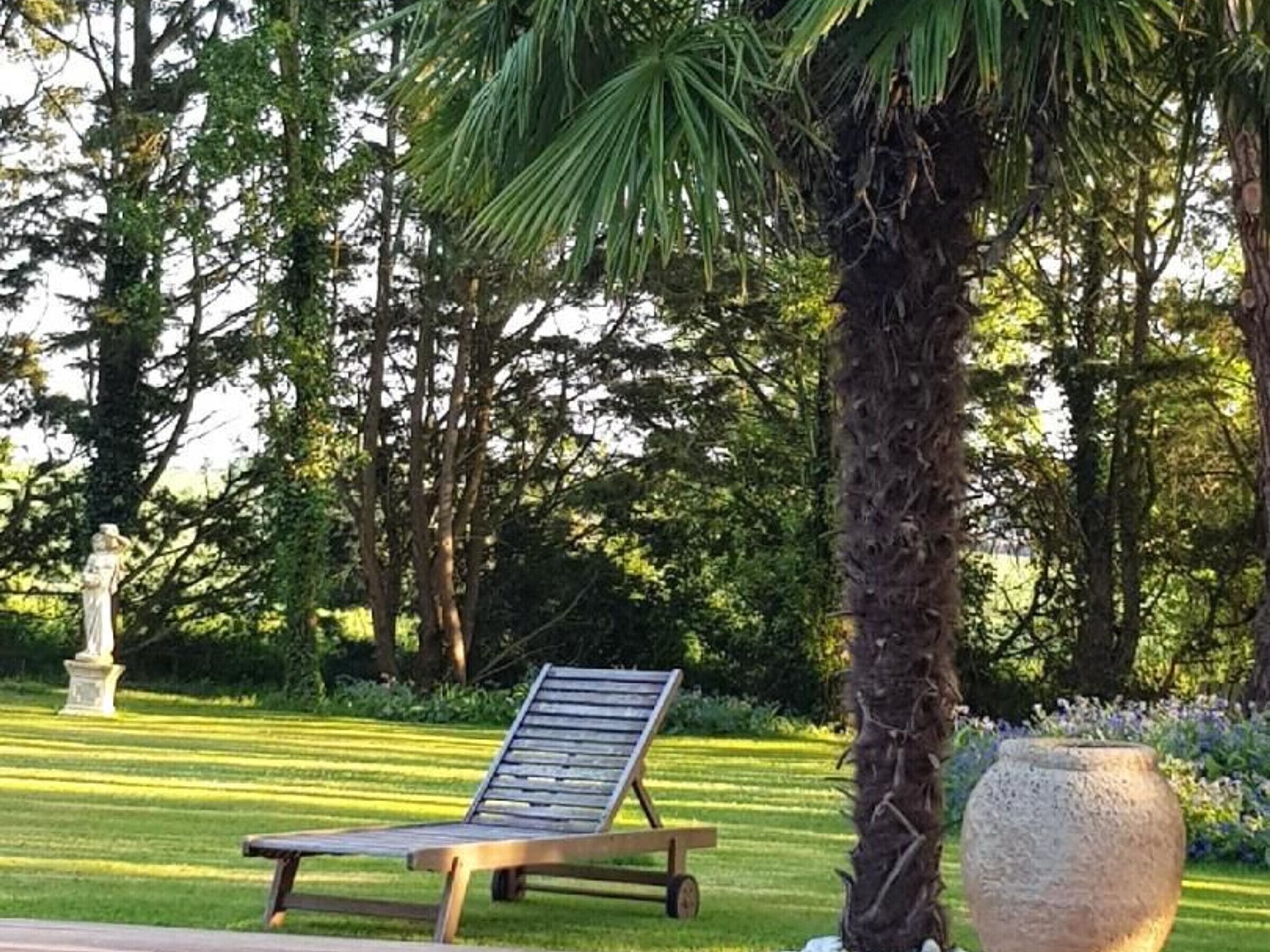A park with a wooden lounge chair, a stone planter, and a statue.