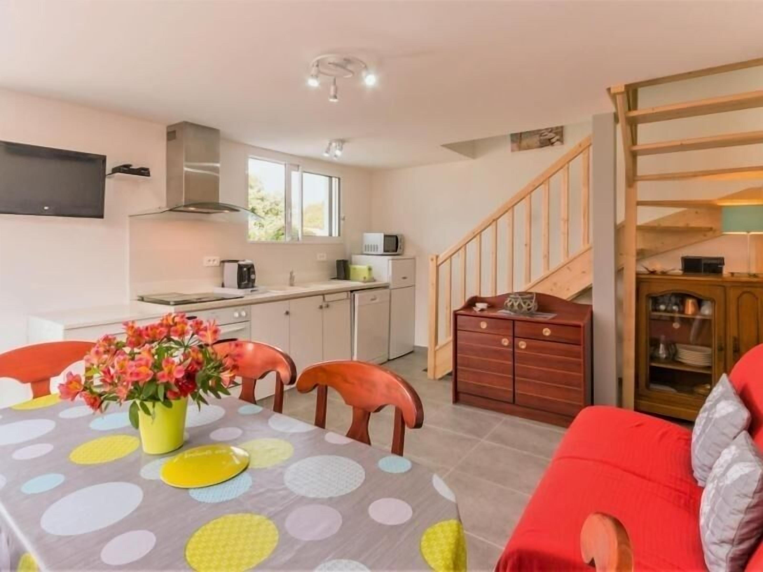 Un espace de vie compact comprenant une table à manger pour deux personnes, un coin cuisine, un canapé et un escalier.