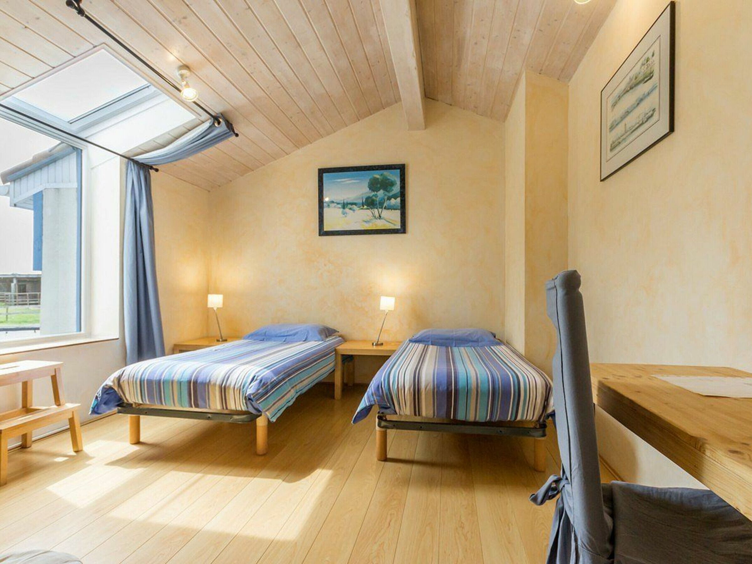 A room with two beds, wooden flooring, a skylight, and a painting on the wall.